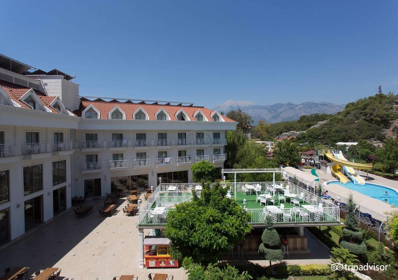 Miramor Hotel & Spa Antalya Exterior foto The photo shows a hotel or resort facility with a well-maintained exterior. There is a large green area with grass and some trees, likely intended for relaxation or recreational activities. In the background, there are water slides suggesting an amus